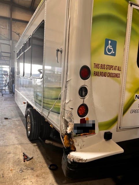 Commercial shuttle bus with severe fiberglass collision damage to the right rear corner before repair