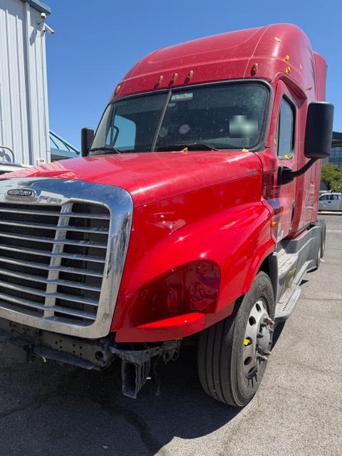 Close-up of collision damage to the driver's side hood and headlight area of a Freightliner Cascadia